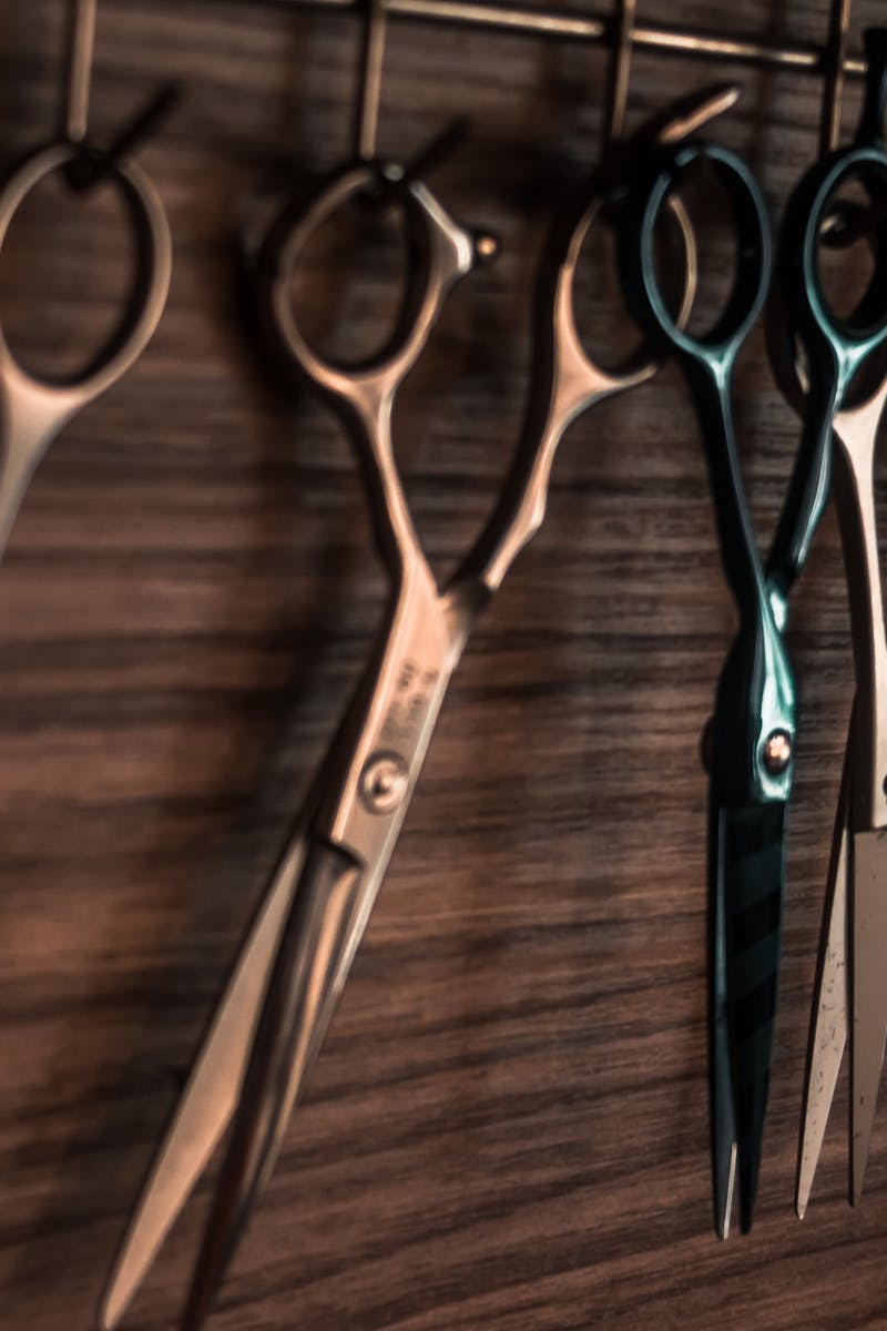 A collection of vintage barber scissors hanging on a wooden wall, showcasing sharp tools for hair cutting.